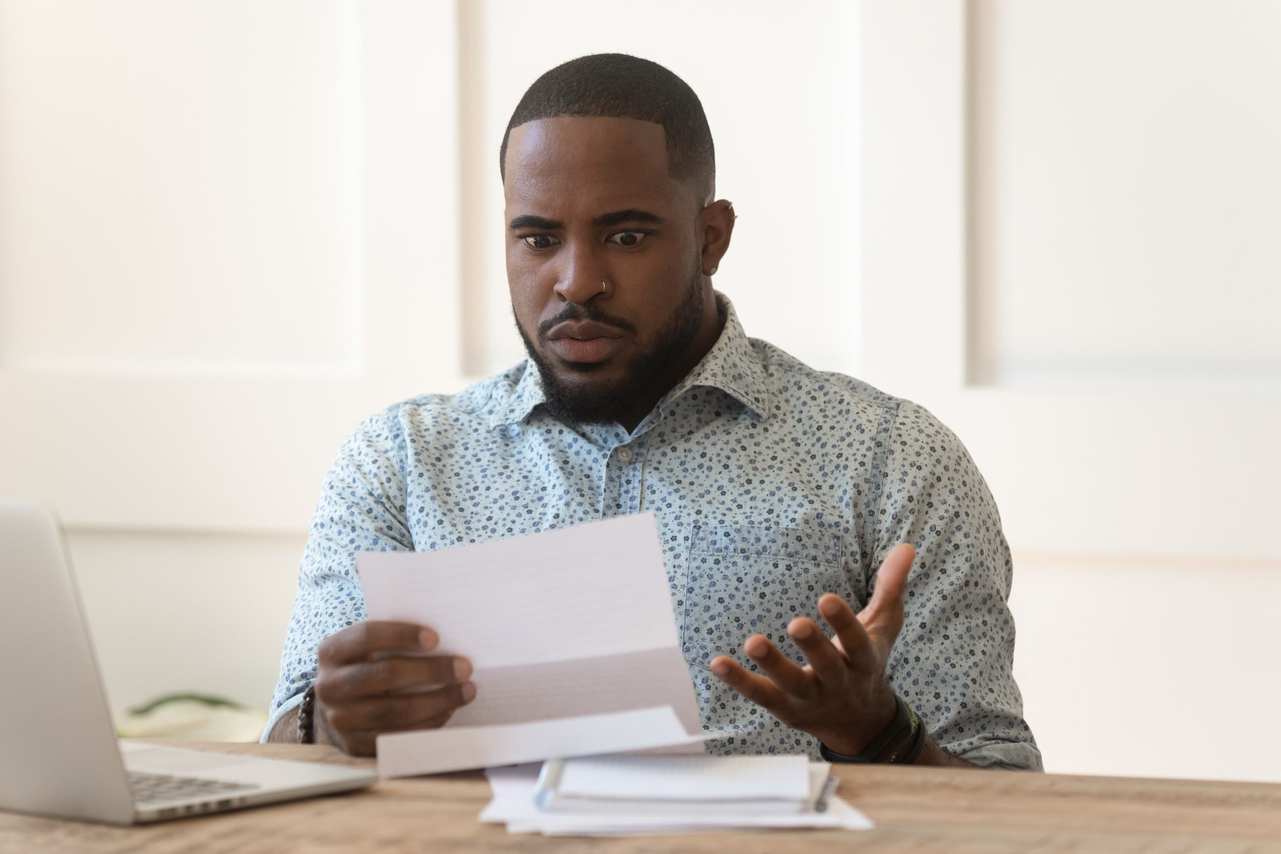 Small business owner surprised reading IRS notice or tax bill at desk with laptop and paperwork