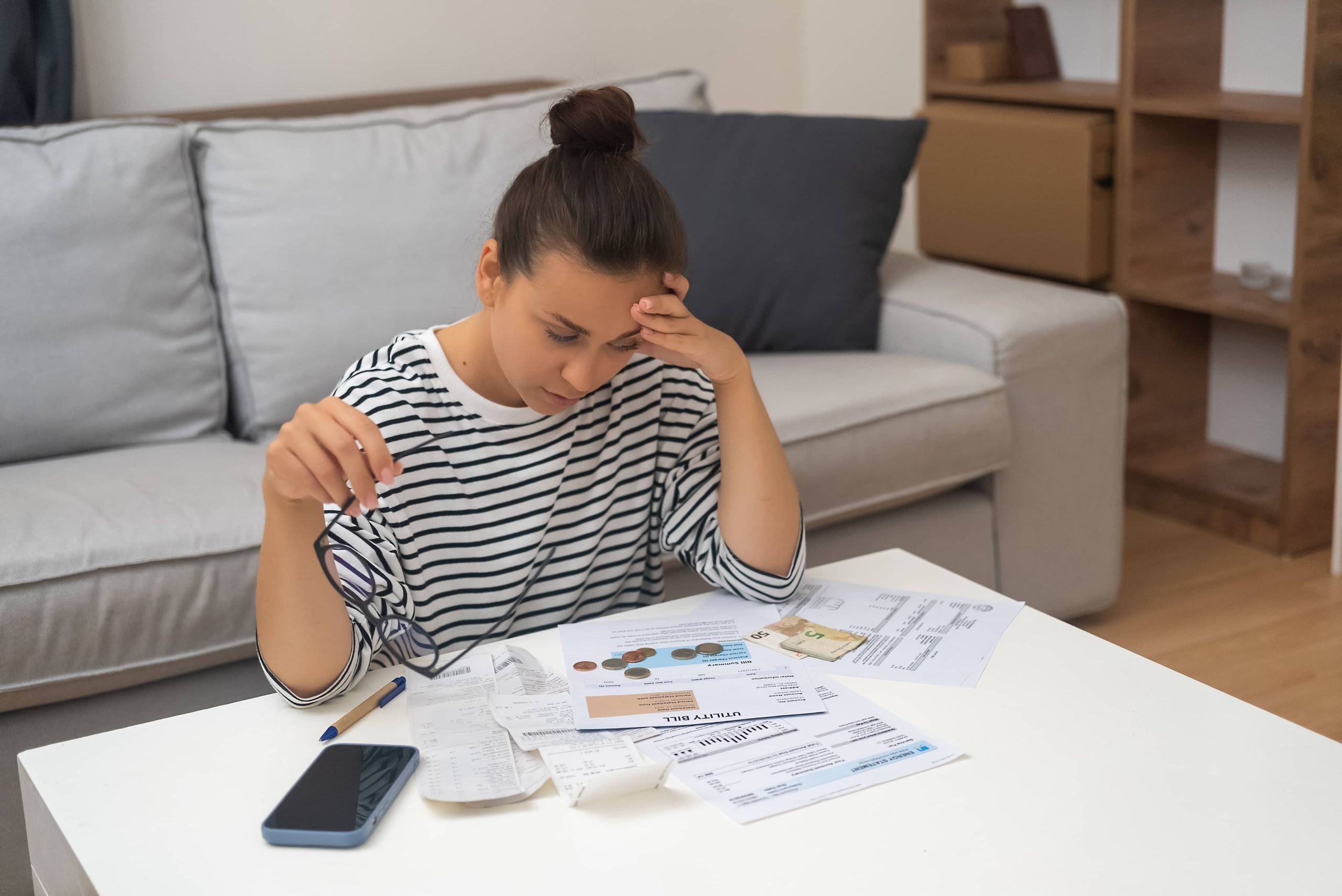 Woman sitting at a table reviewing bills and receipts with a stressed expression while managing personal finances