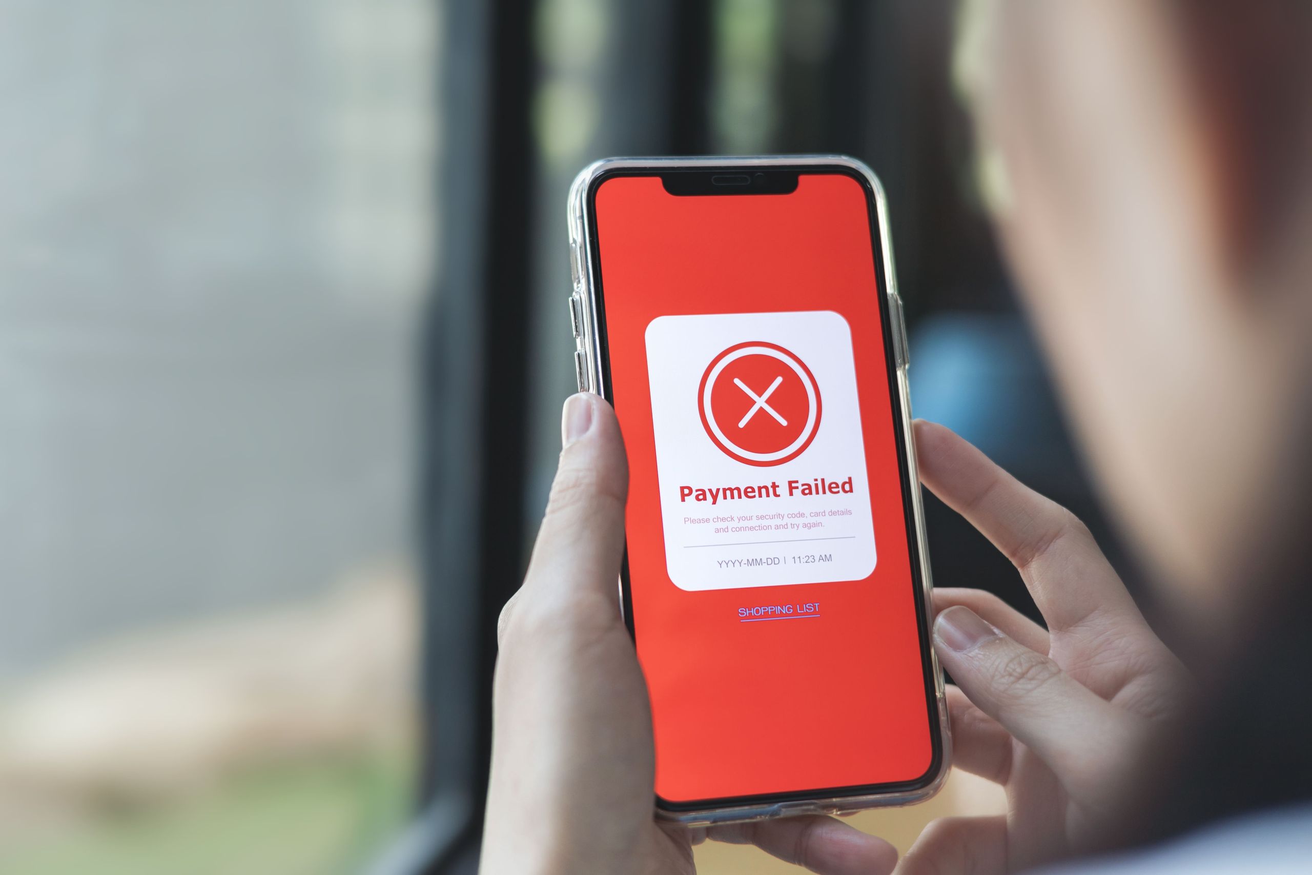 Person holding a smartphone displaying a “Payment Failed” error message on a red screen during an online transaction
